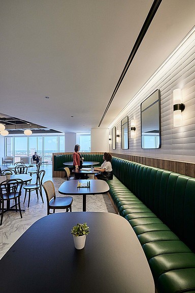 A couple of people sitting at a table in a large room with green couches and a large.