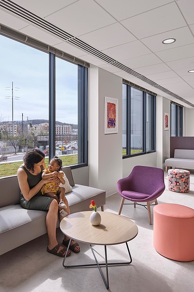 A person and a child sitting on a couch in a room with a window and a view of.