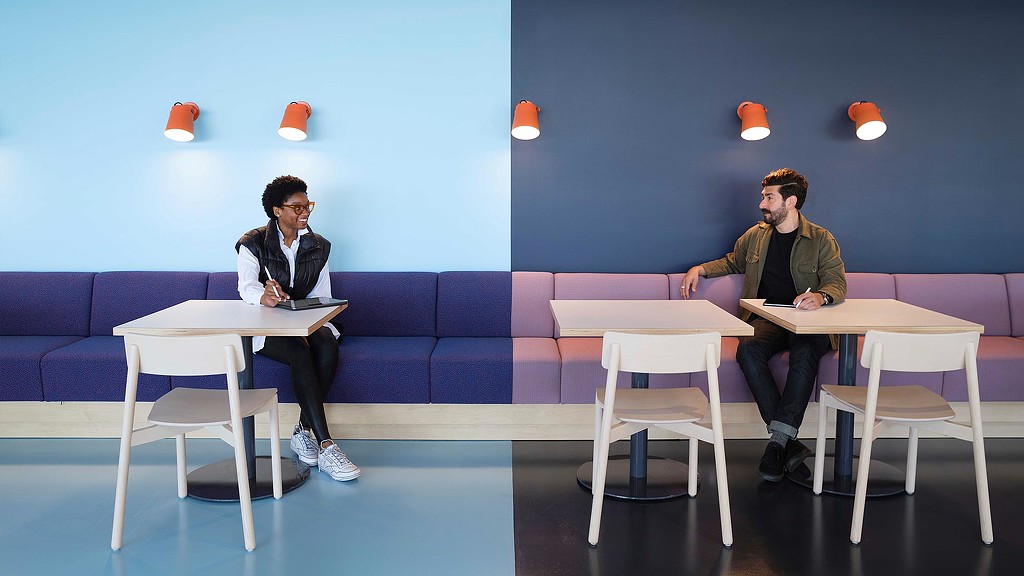 A woman and man sitting on opposite ends of wall seating with blue colorblock wall.