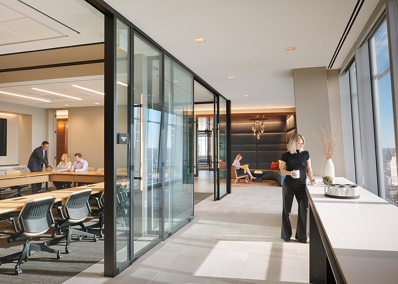 A person standing in a room with people sitting at tables and chairs.
