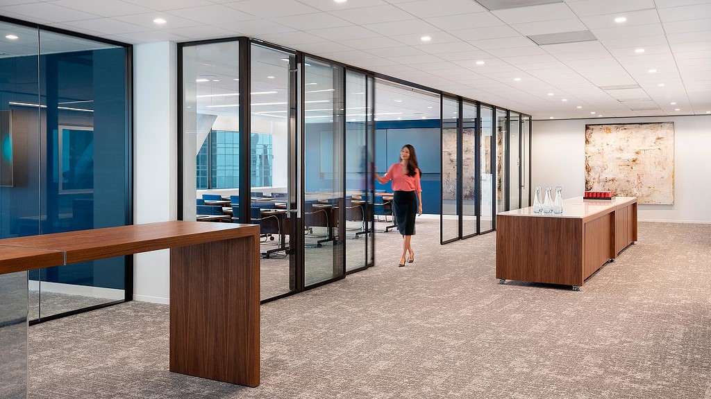 A woman opening sliding conference room glass door at Akin Gump Houston.