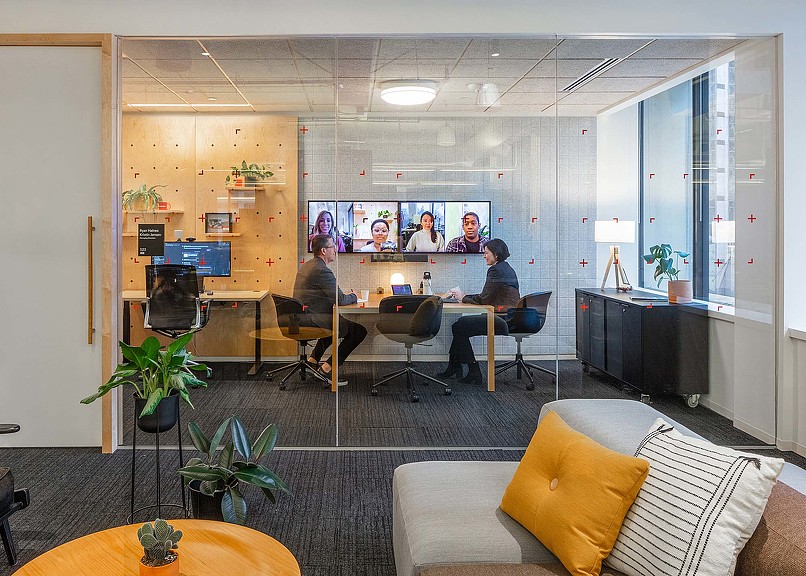 A group of people sitting at a table in a room with a large screen.