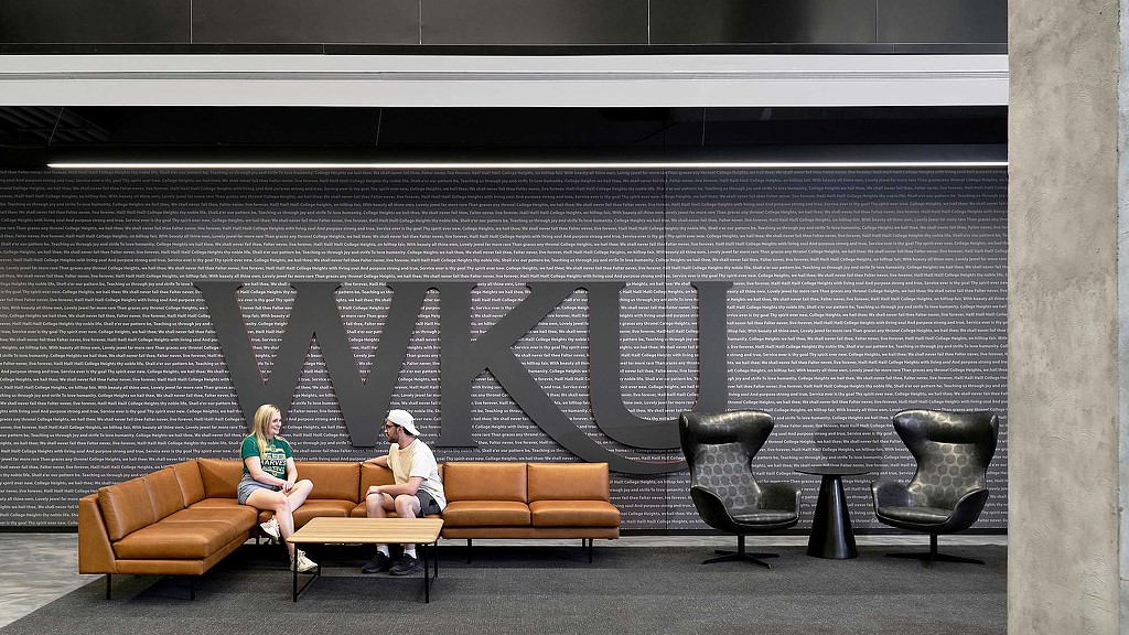 A man and a woman sitting on a couch in front of a wall with environmental graphic design at Kentucky University Commons Helm Library