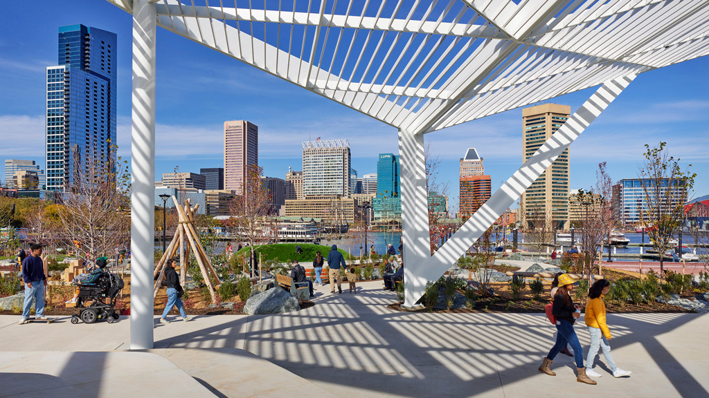 A group of people walking around a large structure with a city in the background.