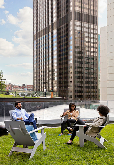 A group of people sitting outside on a rooftop lawn in a city at United Airlines lounge