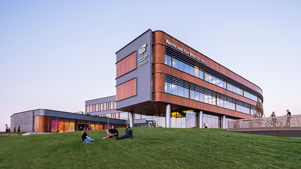 People sitting on the grass outside the warm wooden facade of the Wichita State University Business School in Kansas