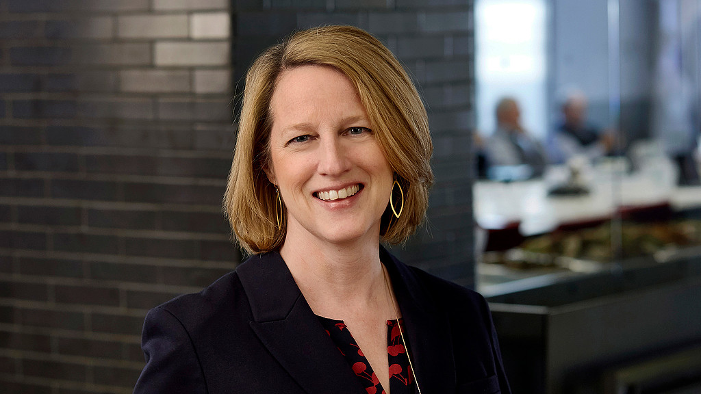A person smiling in front of a brick wall.
