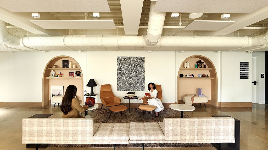 A couple of women sitting in a room with a large screen and a table with chairs and a.