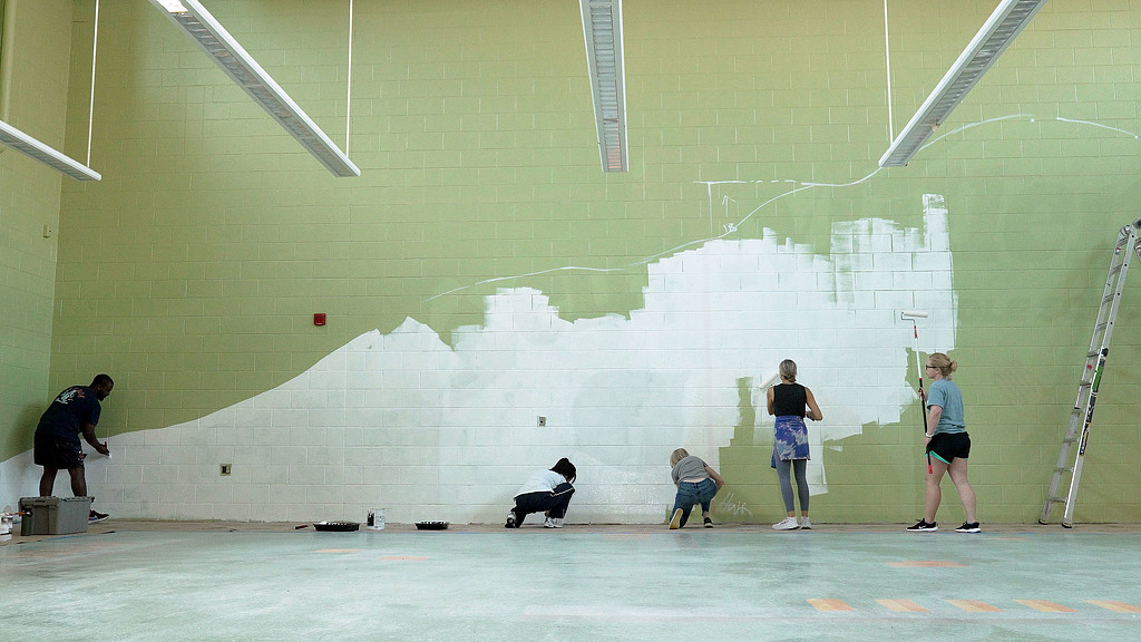 5 team members painting Kelly Miller Middle School cafeteria wall