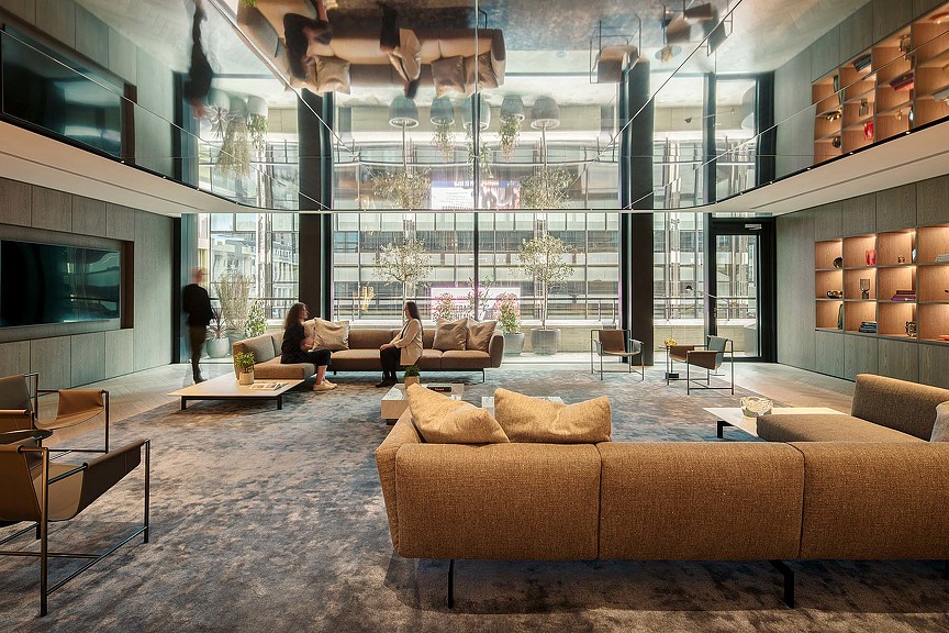 A room with a large glass wall and a couple of people sitting on couches.