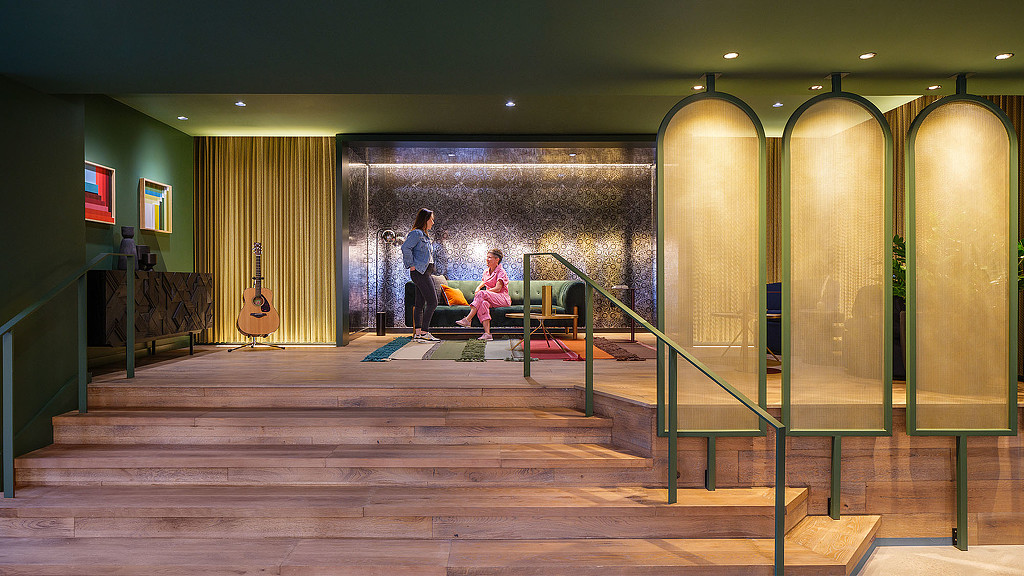 A couple of people sitting on a bench in a room with green walls.