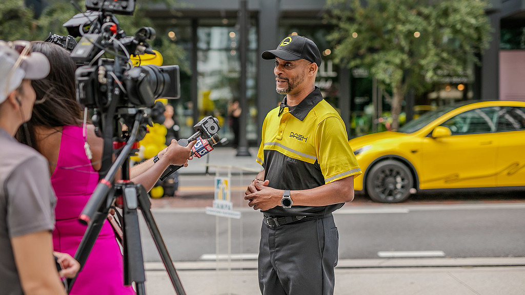 A man in DASH branded shirt and cap being interviewed on the sidewalk