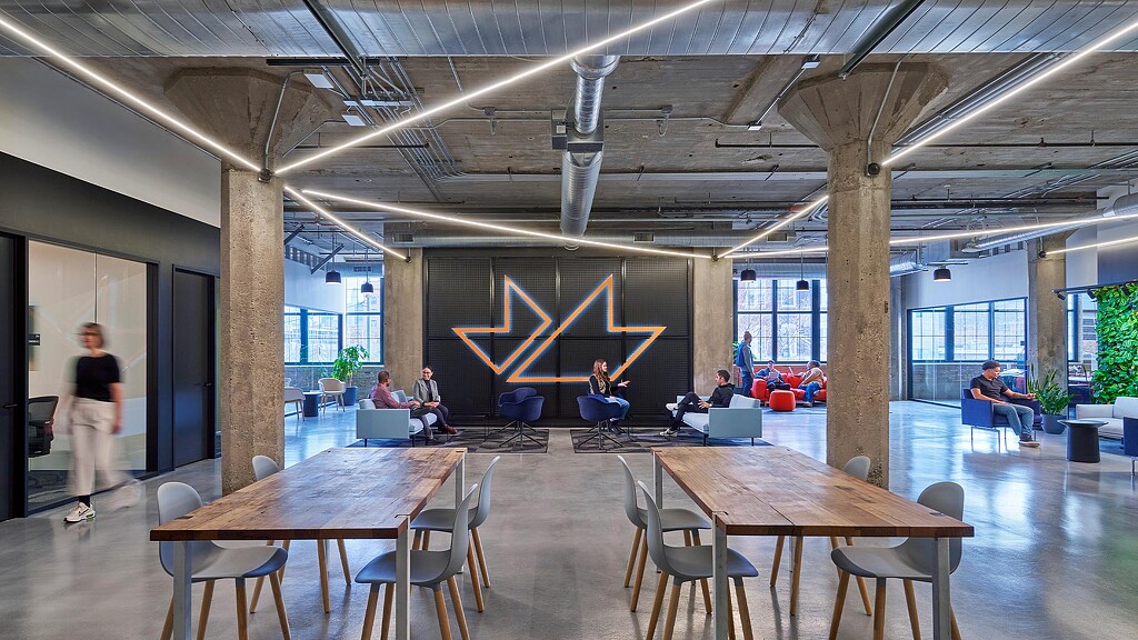 A group of people sitting at tables in a large room with windows.