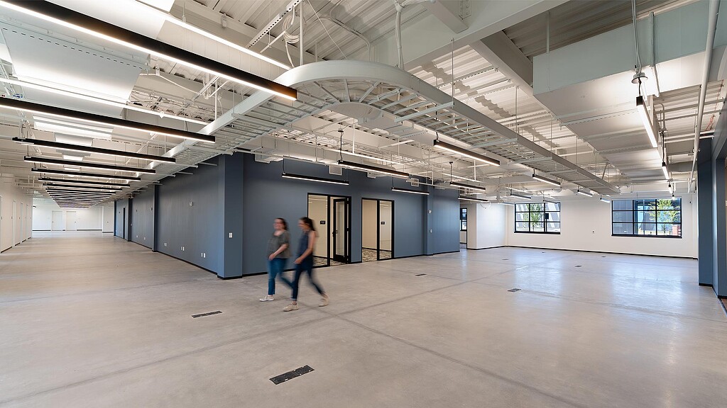 A couple of men walking in a large empty room.