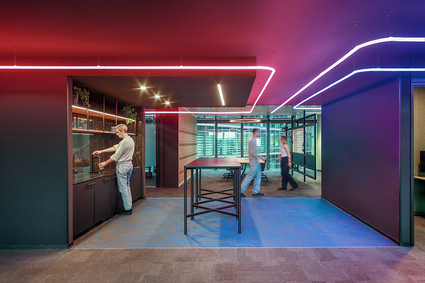 A group of people standing in a room with a table and a purple wall.
