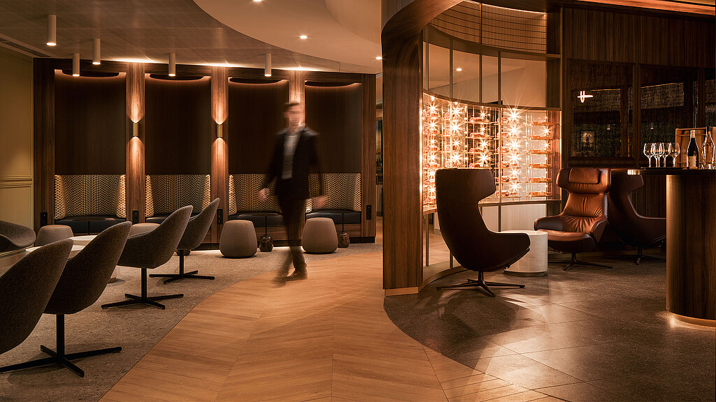 A person walking in a room with chairs and a large window.