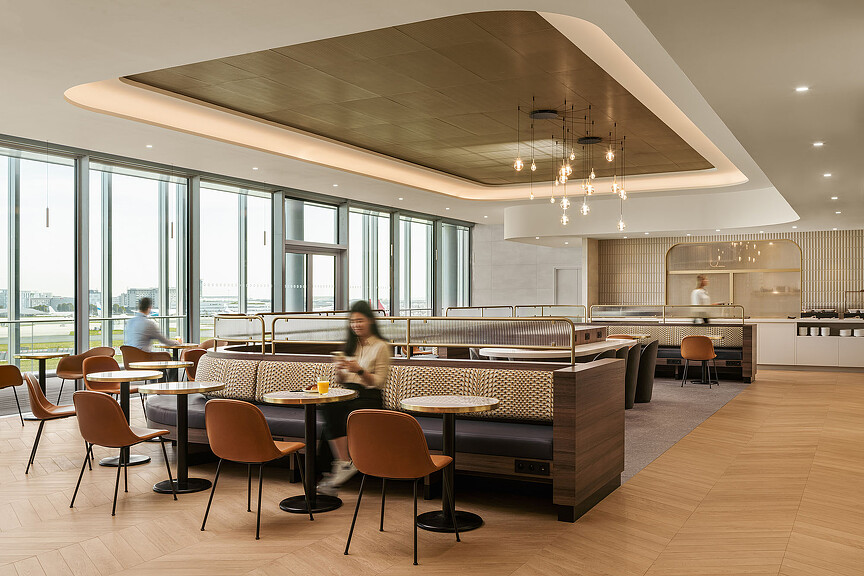 A couple of people sitting at a table in a large room with large windows.