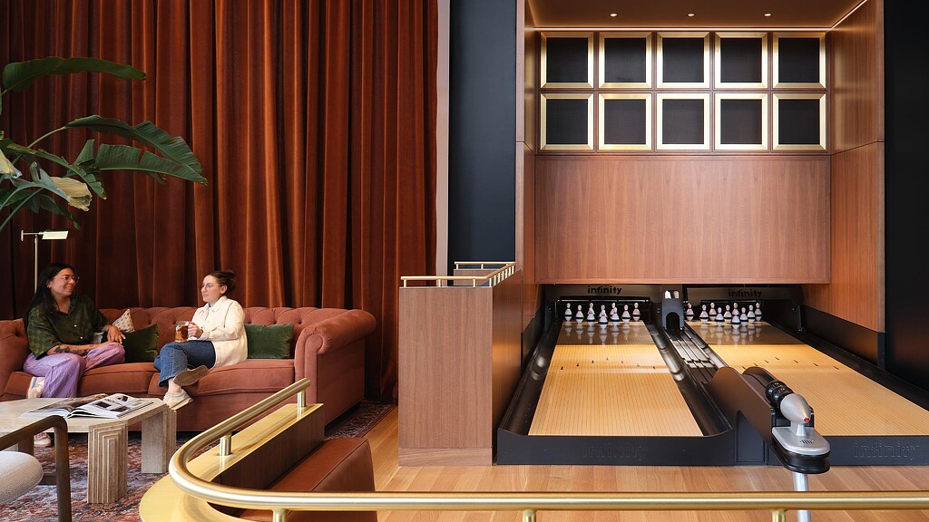 A man and woman sitting on a couch in a room with a large screen and a table.