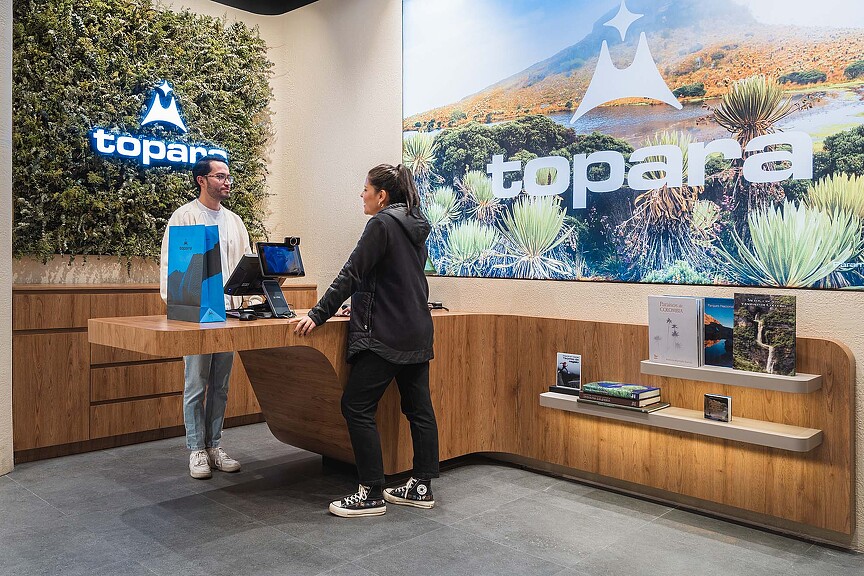 A man and woman standing at a counter with a laptop and a large poster on the wall.