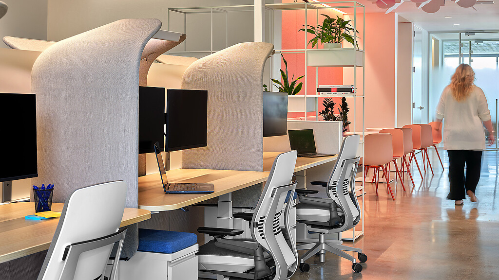 A person walking in a room with a computer and chairs.