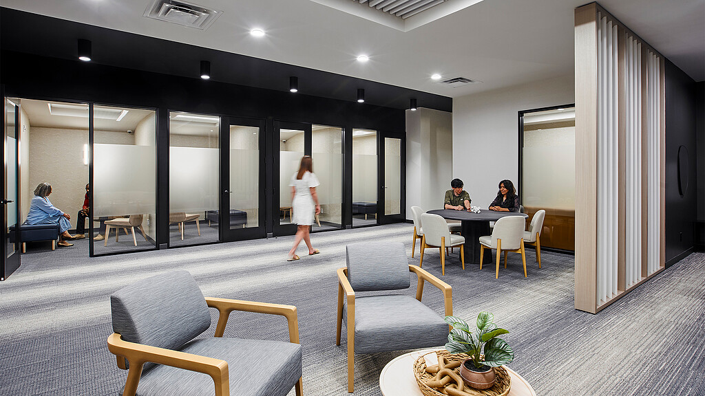 A person standing in a room with chairs and a table with people sitting at it.