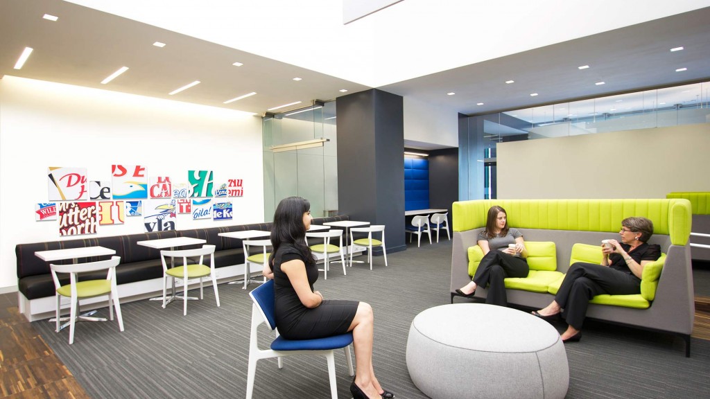 A group of people sitting on green couches in a room.