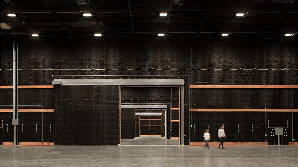 A couple of people walking in a large room with black walls.