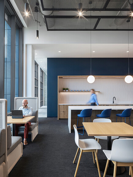 A man and a woman sitting at a table in a room with blue chairs and a white wall.