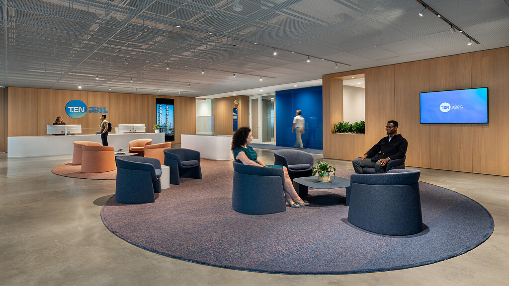 A group of people sitting in a room with blue chairs and a large screen.