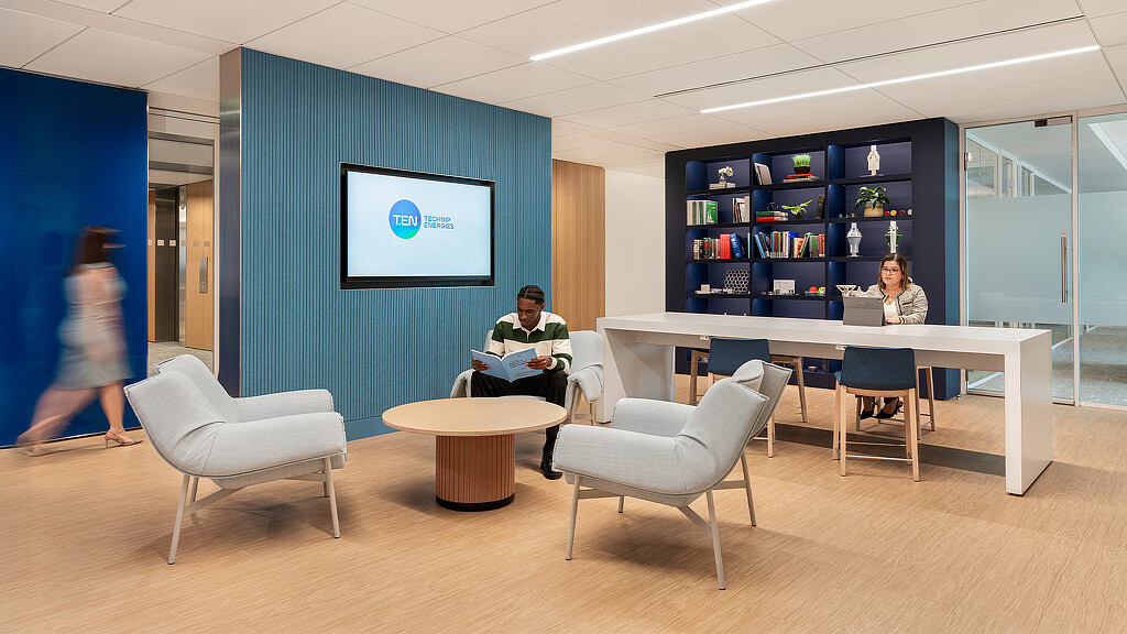 A man and woman sitting at a table in a room with a large screen and a large book.