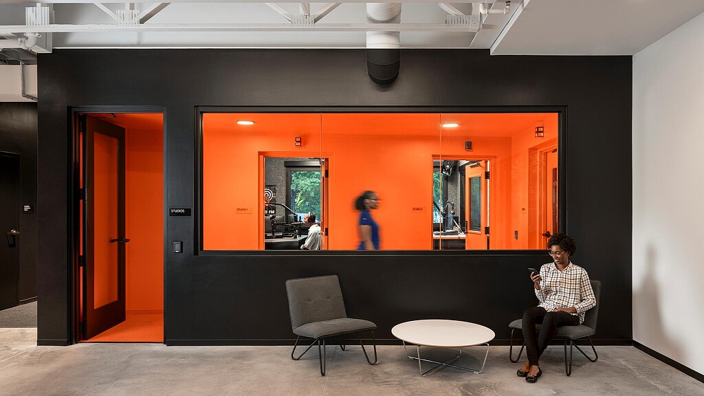 A man and woman sitting in a room with a large orange wall.