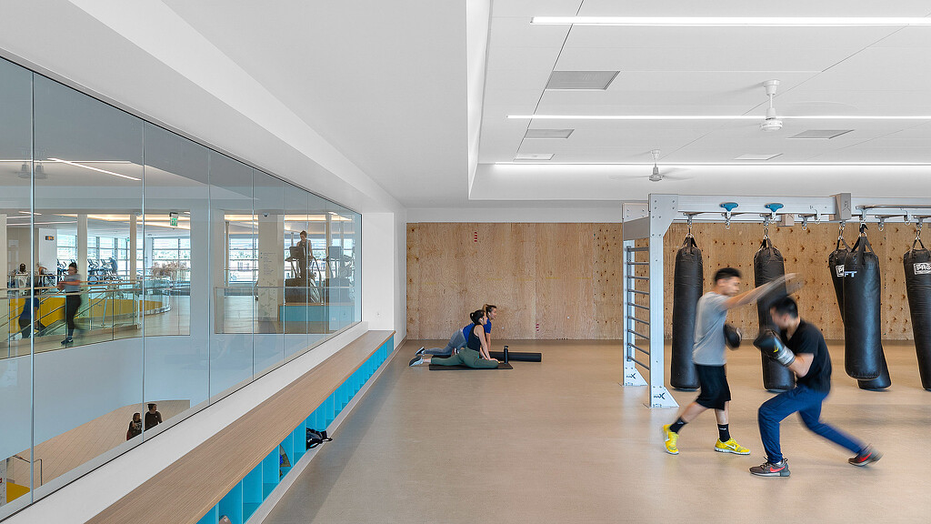 People in a room with a glass wall and a person sitting on a bench.