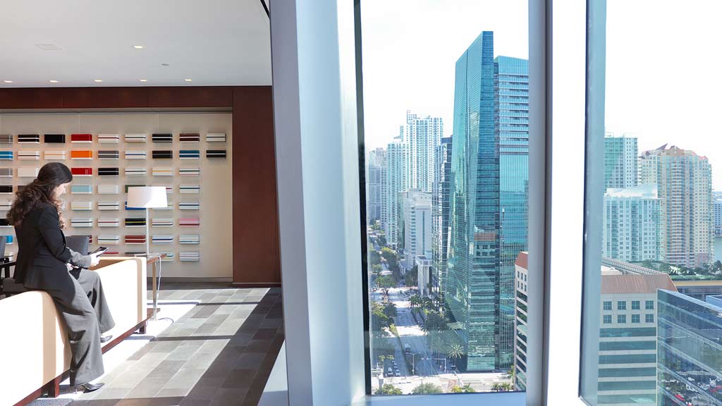 A person sitting on a ledge looking out a window at a city.