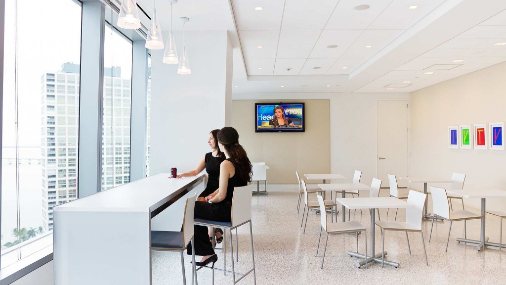 A couple of women sitting at a table in a room with a large window and a large screen.
