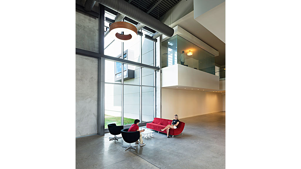 A couple of people sitting on a couch in a room with large windows.