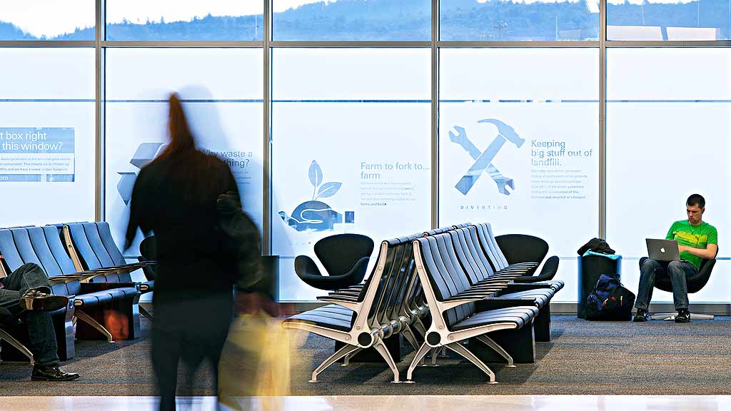 A person standing in front of a window with a laptop and people sitting in chairs.