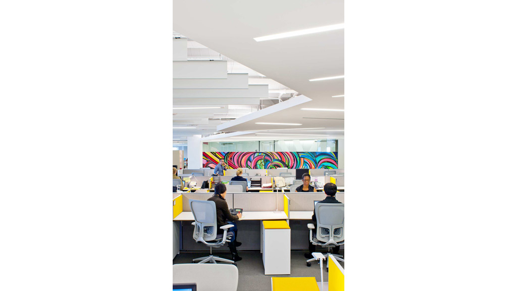 A group of people sitting at desks in a room with a large colorful wall.