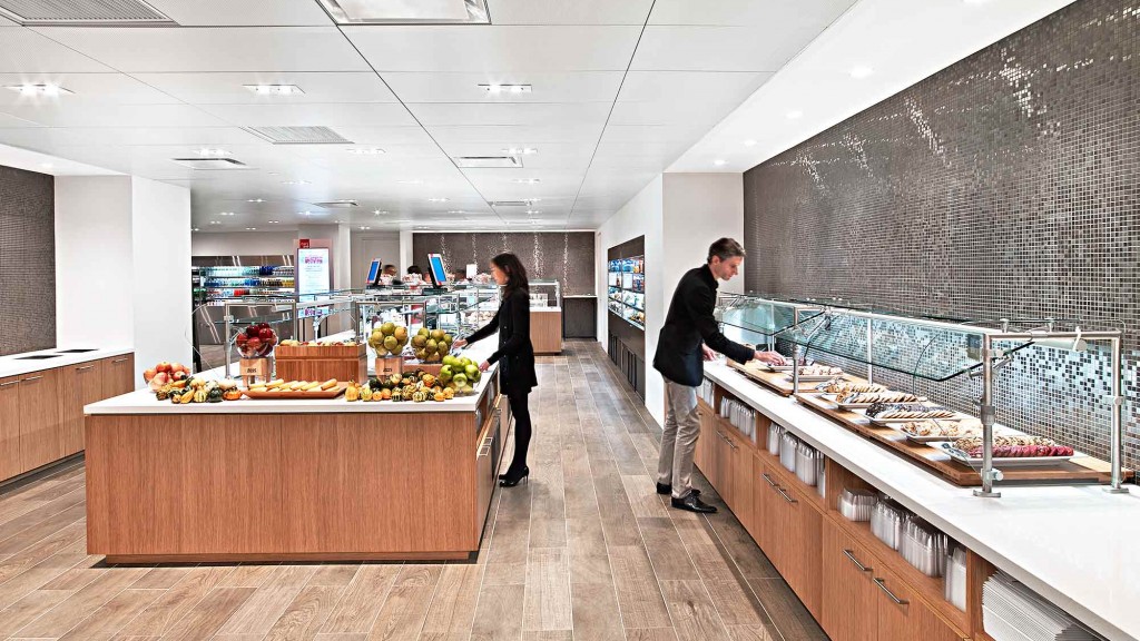 A man and woman standing in a large room with food on the counter.