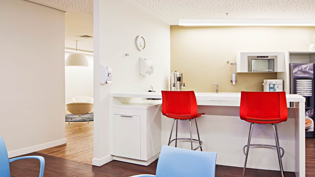 A room with red chairs and a table with a white table and a white wall with a clock.
