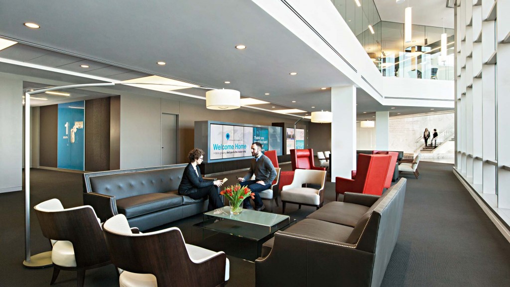 A man and woman sitting on a couch in a room with a large screen.