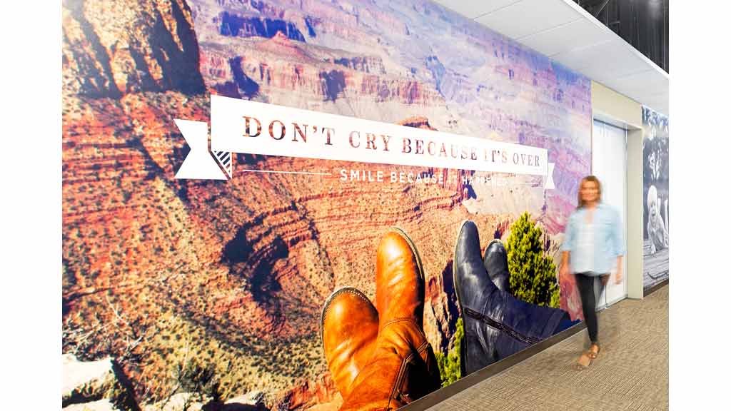 A man walking next to a wall with art on it.