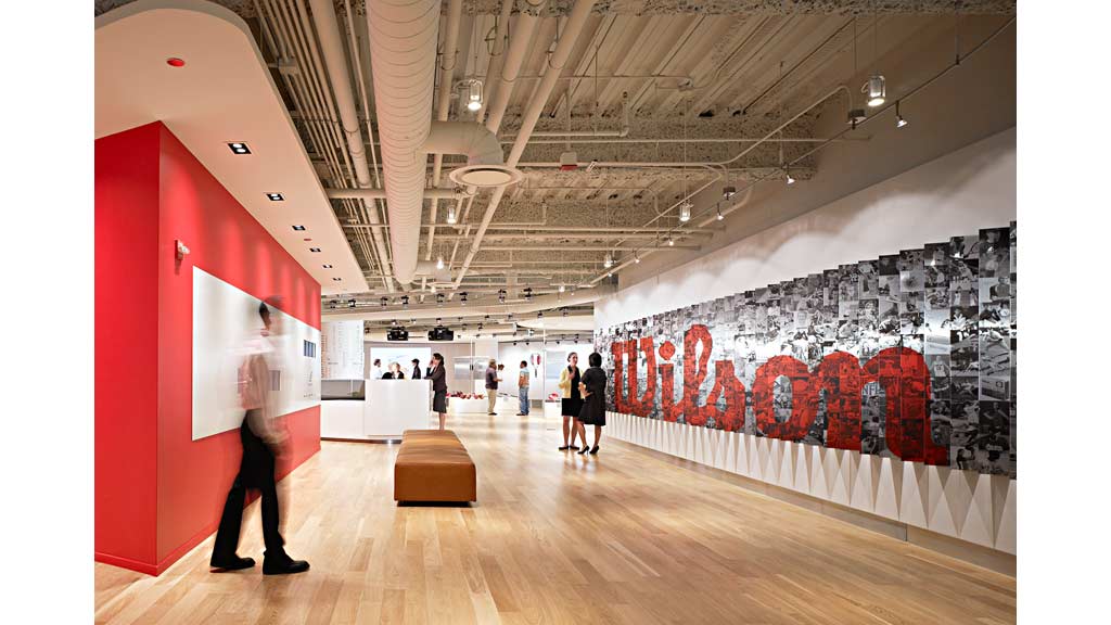 A group of people in a large room with a large red wall.
