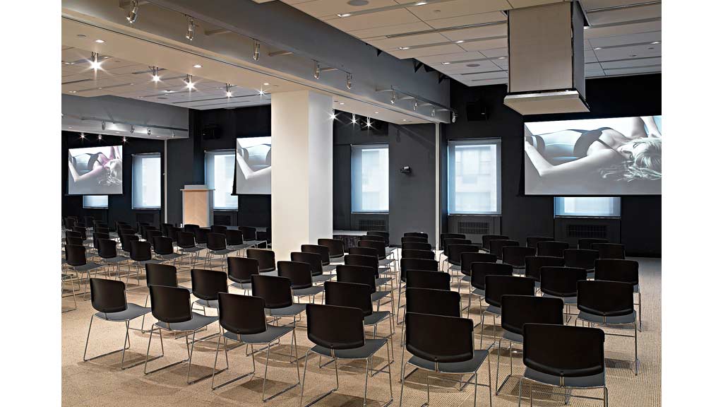 A room with a large group of chairs and a stage with a screen.
