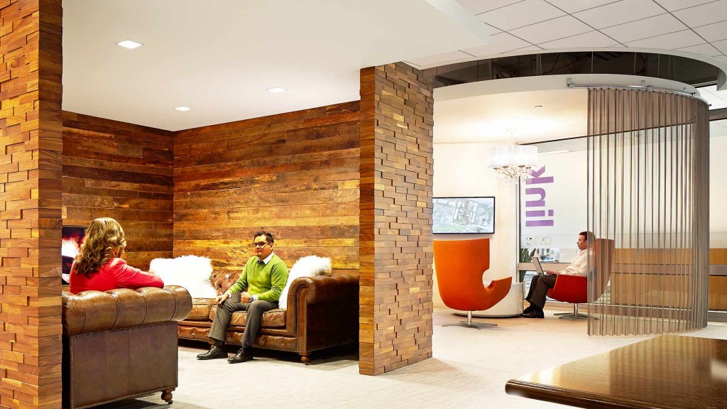 A man and woman sitting on a couch in a room with a brick wall and a glass door.