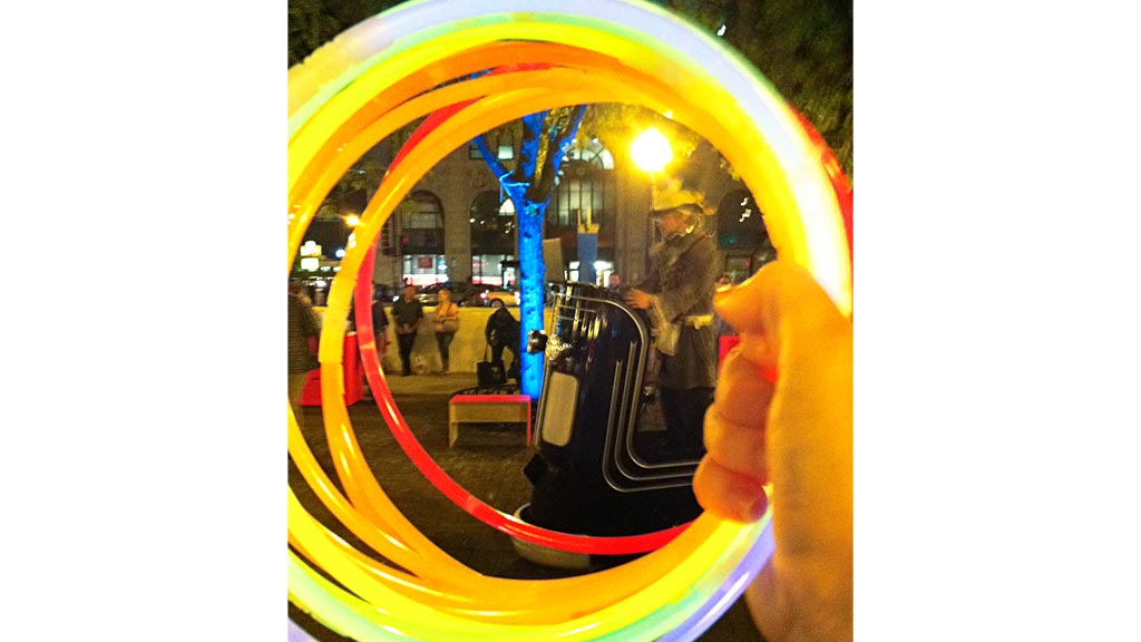 A hand holding a mirror with a person in a hat in the background.