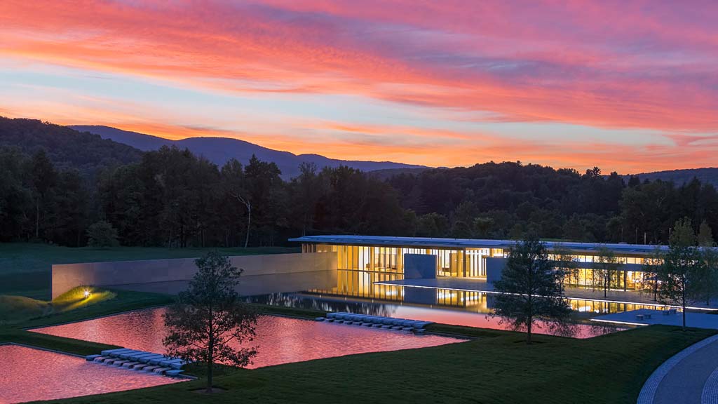 A building with a pool in front of it and trees in the back.