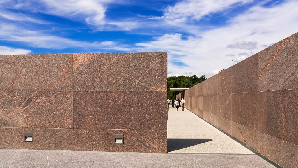 A group of people walking on a paved area next to a brick wall.