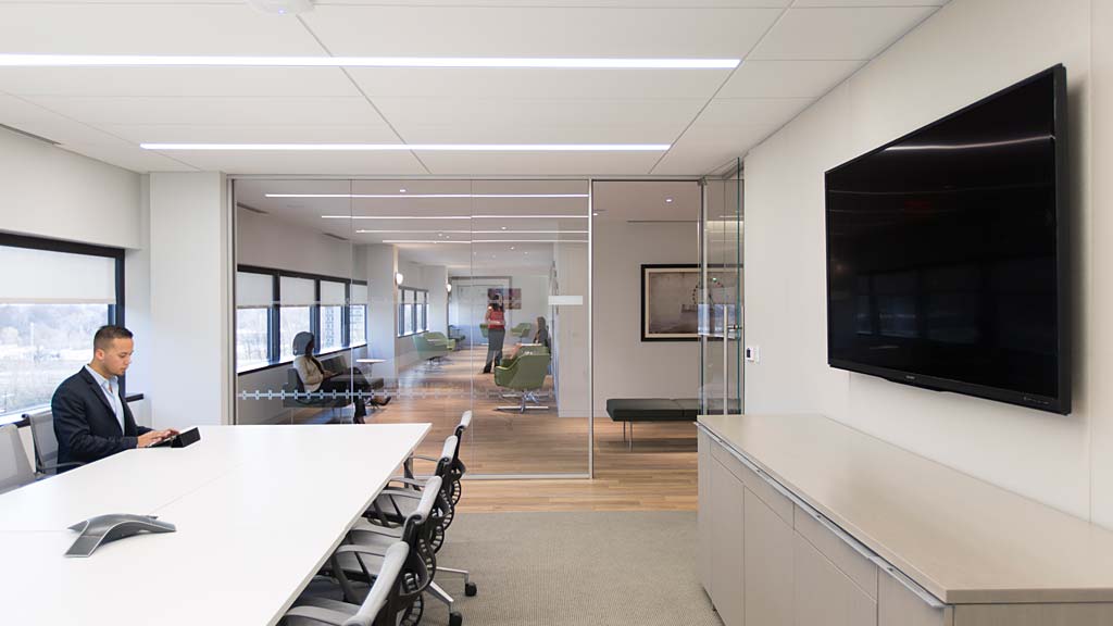 A person sitting at a table in a room with a large screen.