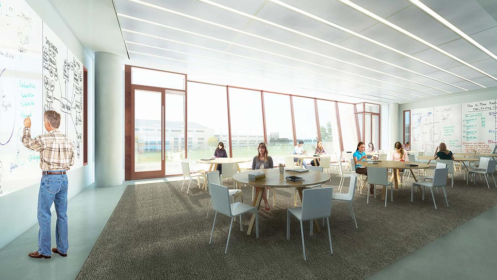 A person standing in a room with people sitting at tables and a large window.