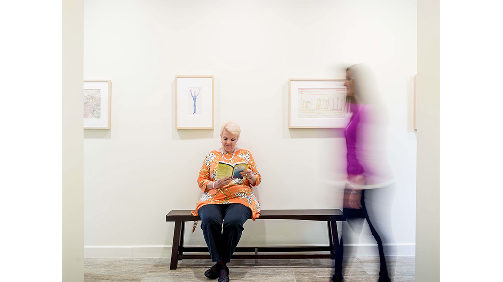 A woman standing next to a man sitting on a bench.